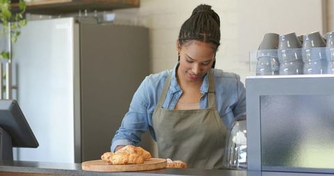 Barista arranging croissants on wooden board behind modern cafe counter