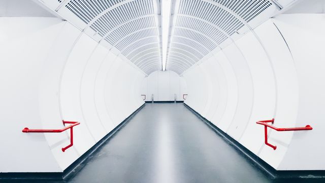 This tunnel has a sleek and futuristic design, perfectly suited for presentations on modern architecture. The minimalist white hallway with striking red handrails could be used for editorial features, blog posts, or marketing materials focusing on contemporary design elements, innovation, or advanced transportation pathways.