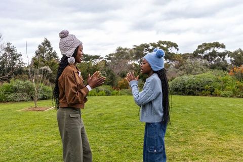 African american preteen girls playing hand-clap game on green lawn wearing pom-pom hats
