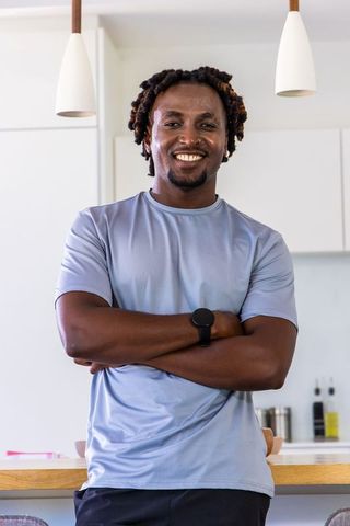 Smiling man standing with arms crossed in modern kitchen wearing athletic tee