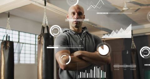Bald boxing coach standing arms folded in gym with performance analytics hud charts