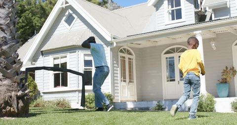 African american father and son playing on sunny suburban lawn by white porch and palm