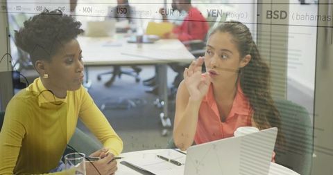 Two professional women collaborating over laptop and documents in modern office meeting