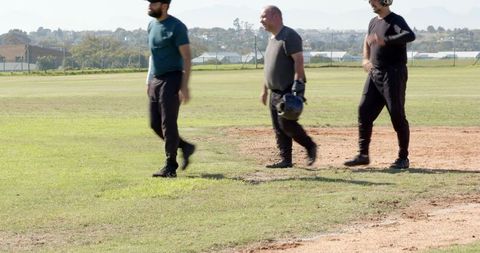 Three Teammates Walking Infield Carrying Helmets and Glove on Sunny Baseball Field Candid