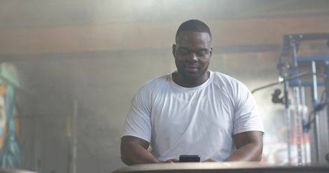 Muscular man checking smartphone after workout in industrial gym with graffiti backdrop