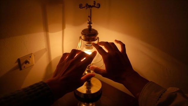 Warming hands over vintage glass lamp glowing amber on wooden bedside table corner
