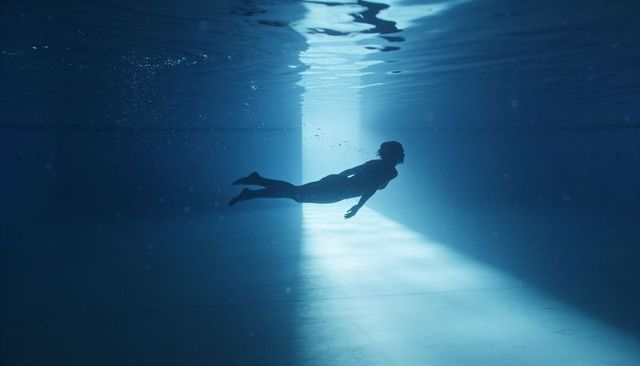 Gliding male swimmer backlit by beam of light in deep blue pool