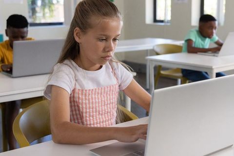 Focused girl using laptop in diverse classroom learning with edtech and modern devices