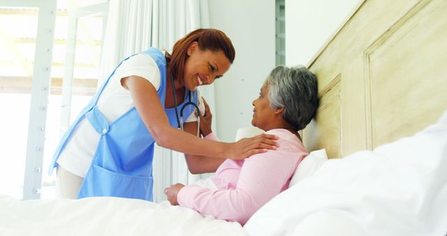 A young African American nurse is attending to a senior patient in a bright bedroom, with copy space. Her caring approach reflects the compassionate nature of healthcare professionals in patient recovery.