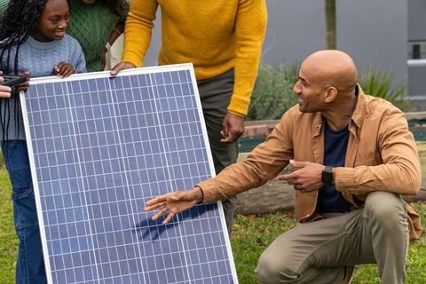 Diverse family inspecting solar panel in backyard, African American girl holding smartphone