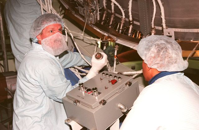 Two NASA scientists in protective clothing are checking and preparing equipment vital for the STS-97 mission inside the Space Station Processing Facility. This image, taken in 1999, captures the meticulous pre-launch activities required to ensure the functionality and safety of the integrated truss structure P6 that was to be launched. This stock photo is ideal for educational materials, articles or presentations about NASA missions, space technology, aerospace procedures, and international space collaboration.