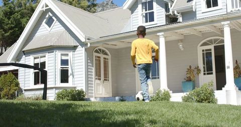 African american boy kicking soccer ball on lawn in front of white porch suburban home