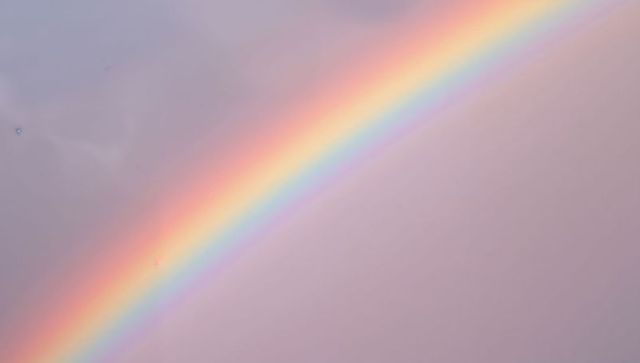 Vibrant diagonal rainbow arc stretching across soft pastel sky after rain shower