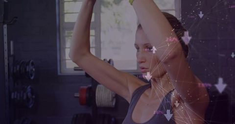 Female athlete raising arms overhead in gym with digital performance data overlay