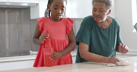 African american grandmother and granddaughter cleaning kitchen counter, family bonding