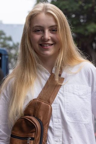Smiling blonde woman wearing white shirt and brown leather crossbody bag on city street
