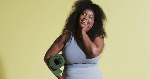 Joyful woman with yoga mat against yellow backdrop