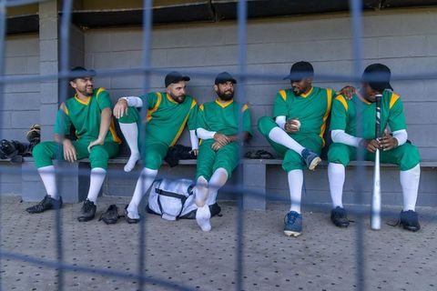 Baseball team relaxing on dugout bench wearing green uniforms preparing for game