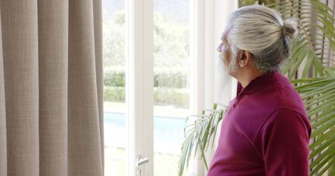Pensive Senior Man Gazing Out Bright Window in Home