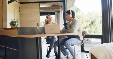 Cohosts recording podcast in cozy rustic kitchen using laptop microphone and headphones