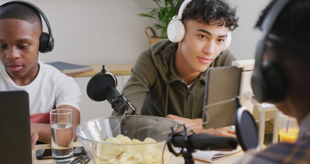 Group of teenagers wearing headphones, recording a podcast in a home studio. Various recording equipment and snacks on the table, showing a collaborative and casual work environment. Ideal for use in topics related to creative work, youth engagement, modern technology, and digital content creation.