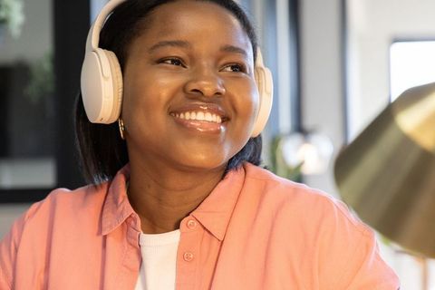 African american teenager smiling while studying with headphones in home office
