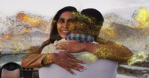 Hugging couple smiling on boat with golden glitter overlay near rocky coastline