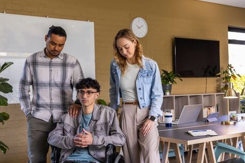 Diverse coworkers supporting colleague in wheelchair during modern office team collaboration