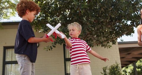 Multiracial children playing with rolled paper batons tied with red ribbon on porch