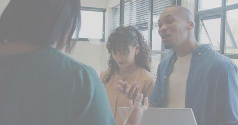 Diverse team collaborating around laptop in bright modern office for teamwork and brainstorming