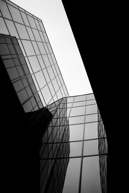Modern skyscraper buildings reflect the sky in a stunning black and white urban composition. Suitable for articles or media exploring city life, architecture, or urban photography. Ideal for use in graphic designs requiring a sleek, sophisticated aesthetic or emphasizing geometric and abstract patterns.