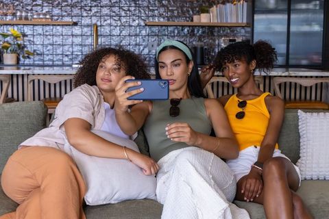 Three friends taking selfie on sofa in trendy café using blue smartphone