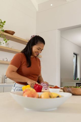 Mid-adult asian woman chopping vegetables on minimal kitchen island with natural light