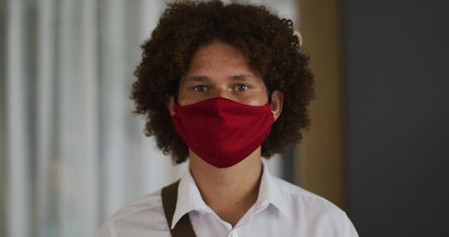 Portrait of biracial man with curly hair wearing red face mask. out and about during coronavirus covid 19 pandemic.