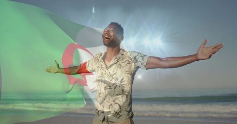 Man celebrating on beach with algerian flag overlay, wearing tropical shirt, sunlit joy