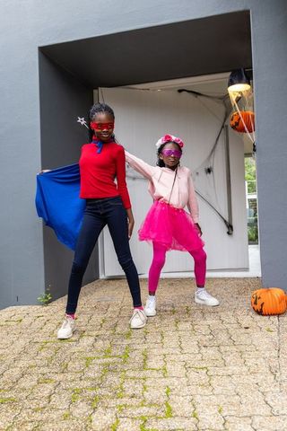 African american girls posing as superheroes in colorful costumes at halloween doorstep