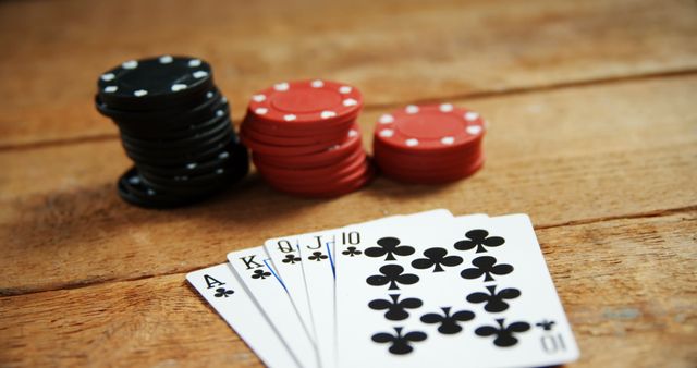 Poker chips and a royal flush in clubs arranged on a wooden table. Ideal for use in gambling themes, casino promotions, game strategies, and entertainment content.