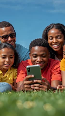 Vertical video of teen tapping smartphone while family laughing on grassy field