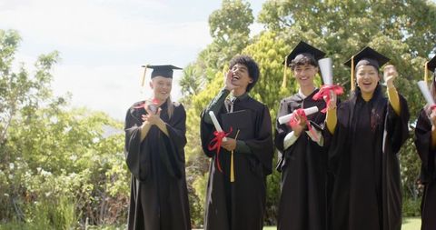 Diverse graduates celebrating on campus lawn holding diplomas and wearing mortarboards
