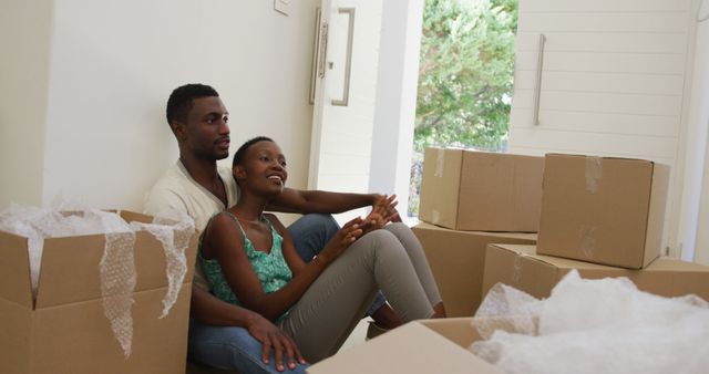 Happy african american couple embracing and talking sitting on floor with packing boxes. moving into a new home.