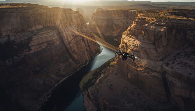 Drone flying over winding sandstone canyon at golden hour with river and sun flare