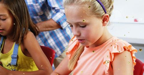 Blonde girl concentrating on school craft project with classmate and mentor