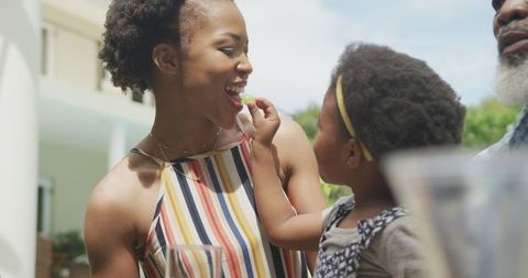 Joyful Family Morning: Child Feeding Mother Outdoors in Sunny Garden