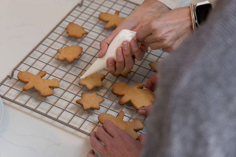 Hands decorating gingerbread cookies with icing bag on cooling rack for holiday baking