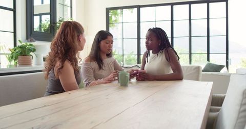 Multiracial friends having heartfelt conversation around sunlit wood dining table