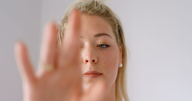 Blonde woman raising her hand, partially covering her face, likely indicating stop or focus. Useful for themes on personal boundaries, mindfulness, body language, or emotional expressions. Suitable for articles, blogs, or advertisements related to self-care, privacy, or mental health.