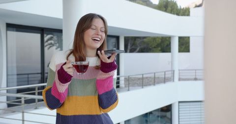 Laughing Woman Taking Voice Message on Balcony Holding Tea