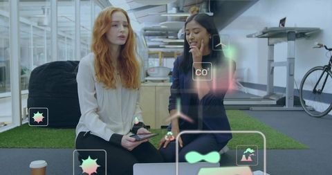 Two women collaborating with augmented reality data overlays in modern coworking office