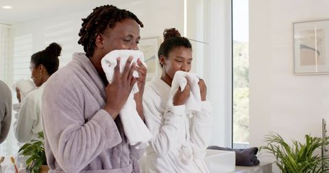African american couple patting faces with towels in bright bathroom morning routine