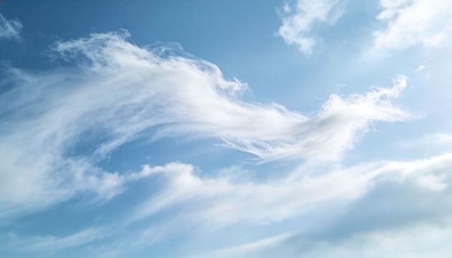 Soft wispy cirrus clouds sweeping across bright blue sky with flowing feather textures
